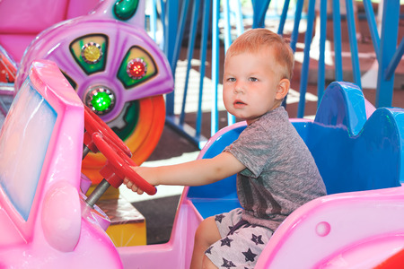 Little boy drives pink children toy car in amusement park summer dayの写真素材