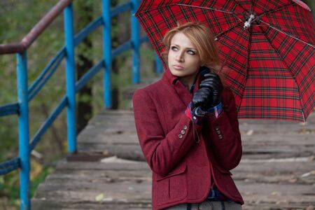 Pretty blond girl in stylish red jacket posing under the checkered umbrellaの写真素材