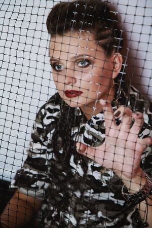 Punk style girl in camouflage jacket looking through metal meshの写真素材