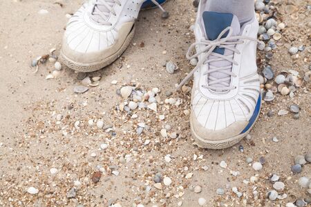 Men feet in old shoes sneakers on the sea beachの写真素材