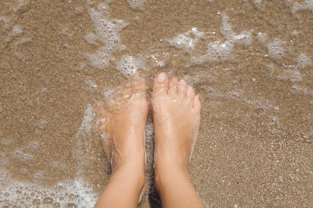 Two female bare feet on wet sand in the sea foamの写真素材