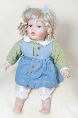 Blue-eyed girl doll with blond hair sitting on a soft light backgroundの写真素材