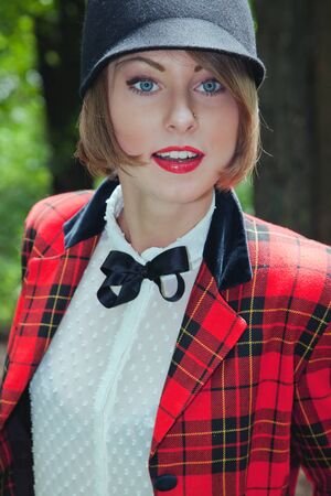 Close-up portrait of beautiful young woman in horsewoman suit in green forest on sunny dayの写真素材