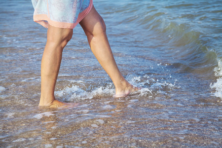Female feet on the sea beach in wave at summer sunny dayの写真素材