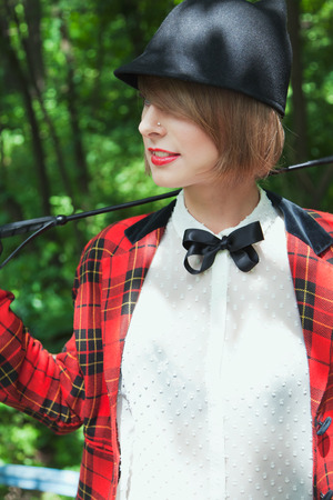 Portrait of beautiful young woman in horsewoman suit in green forest on sunny dayの写真素材