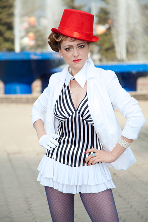 Circus artist woman in red hat posing near fountain outdoorsの写真素材