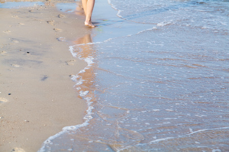 Female feet on the sea beach in wave at summer sunny dayの写真素材