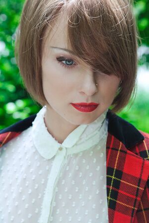 Close-up portrait of beautiful young woman in horsewoman suit in green forest on sunny dayの写真素材