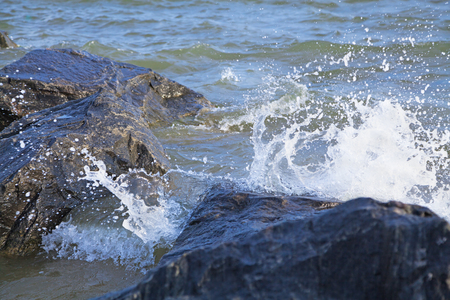 Large boulders on the beach washed by impending wave. Splashes of sea waveの写真素材