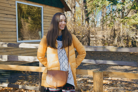 Young beautiful girl stands near the wooden fence in city zoo on sunny autumn dayの写真素材