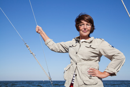 Elderly woman yachtsman on a sailing yacht holds on to the ropes at sunny dayの写真素材