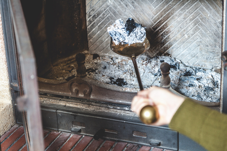 Cleaning the fireplace. Hand of man holding a brass shovel with ashの写真素材