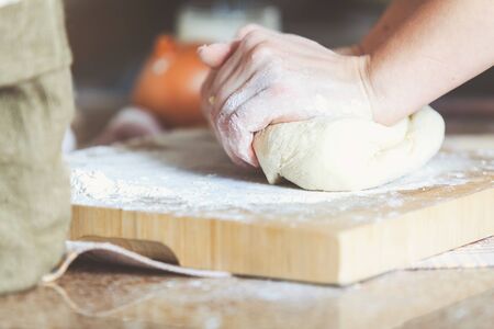 Women hands knead the dough piece on the board with flour. Side view