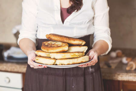 A woman in a skirt holding a plate with a big mouth-watering fried piesの写真素材
