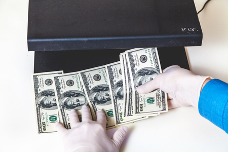 Hands in rubber gloves authenticate dollar bills with a detectorの写真素材