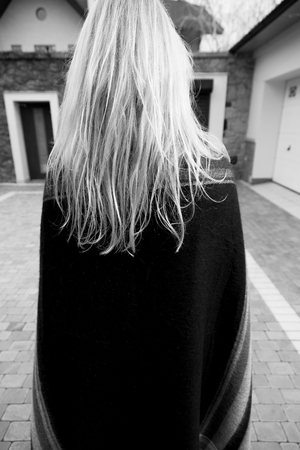 Fashion blond girl with long hair standing in the autumn yard of a private home. View from the back. Monochrome imageの写真素材