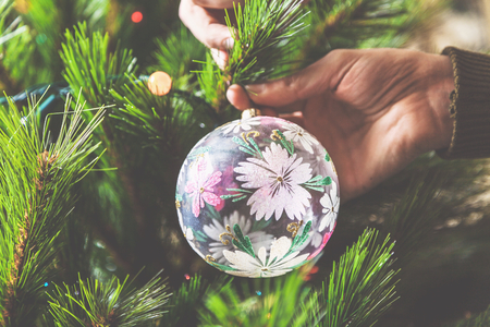 decorate the Christmas tree. men hands hang a glass bowl with a beautiful pattern on a green Christmas tree branchの写真素材