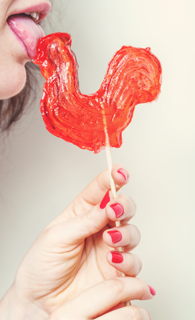 symbol 2017. Cute girl licking candy lollipop red rooster on a white background closeup