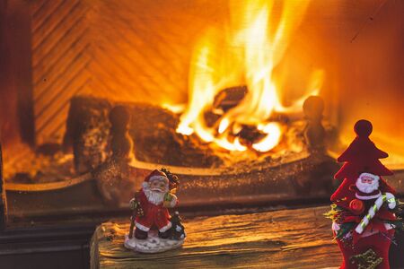 Two figurines of Santa Claus standing on a wooden logs front glass door of a burning fireplace
の写真素材