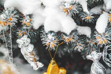 Group of Christmas toys of silver and yellow weigh on green branches snow-covered Christmas tree...