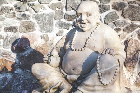 Sculpture Hotei sitting on a background of wall from a natural stone
の写真素材