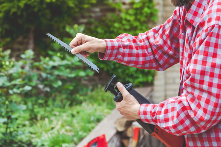 man with a beard in a red plaid shirt inserts a hacksaw in a power saw in the courtyard of a private house
の写真素材