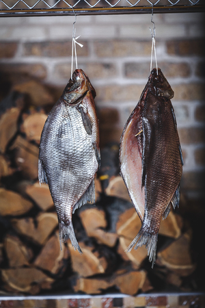 Two large smoked breams are hung on a wooden counter against a brick wall. Firewood is stacked neatly behindの写真素材