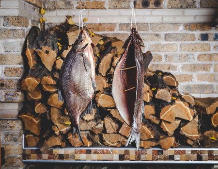 Two large smoked breams are hung on a wooden counter against a brick wall. Firewood is stacked neatly behindの写真素材
