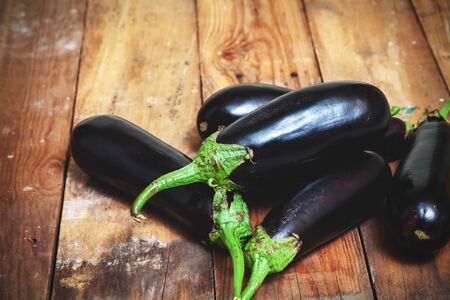group of blue ripe eggplants with green tails lie on old wooden boards planedの写真素材