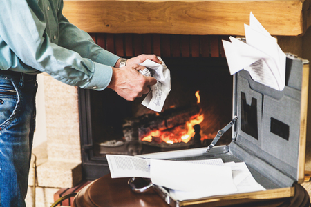 Businessman hands mash paper documents from the case front of a burning fireplaceの写真素材