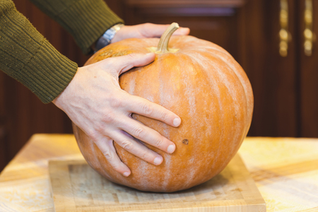 Hands of a man holding a pumpkin on a large round square chopping board closeupの写真素材