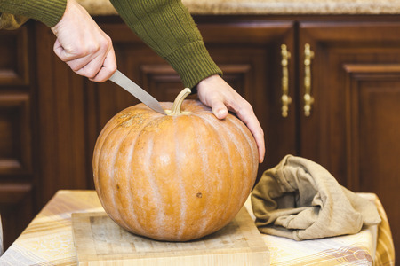 man's hands cut a large round pumpkin with a knife on a square cutting board close-up. There is a canvas bagの写真素材