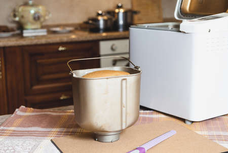 Metal form for baking bread is to stand on a cork table cloths. Inside visible hot loaf of bread. Nearby lies a large knife and white bread makerの写真素材