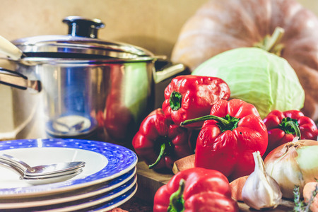 Kitchen still life. Deep bowls, saucepan, pumpkin, cabbage, bell pepper, onion lay on the tableの写真素材