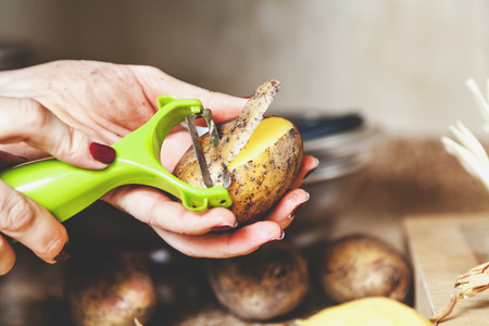 Kitchen work. The hands of a woman with a manicure brush potatoes with a plastic tool with a special blade close-up. Side view
の写真素材