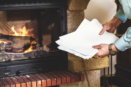 Sheets of white paper in the hands of a man in front of a fireplaceの写真素材