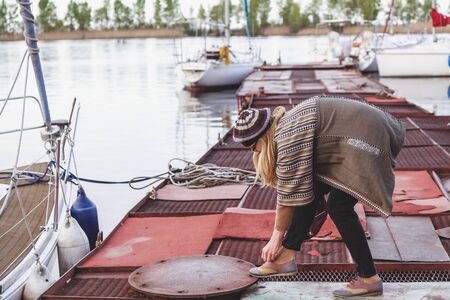 Young blond woman standing on the dock, and tying shoe lace on autumn day 