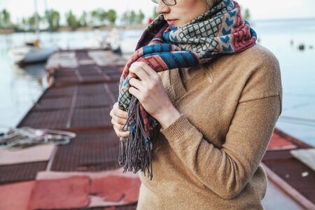 young girl in a sweater tying a knot in the scarf warm autumn dayの写真素材