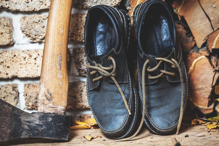 two old boots of the lumberjack are standing vertically on the chopped firewood close-up. Near the big axの写真素材