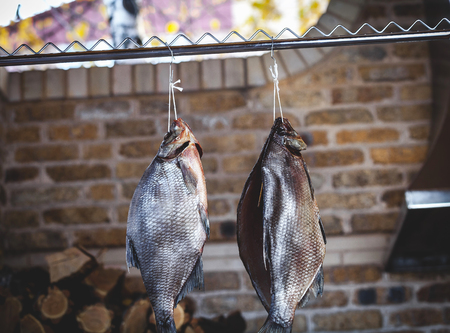 Two large smoked breams are hung on a wooden counter against a brick wall. Firewood is stacked neatly behindの写真素材