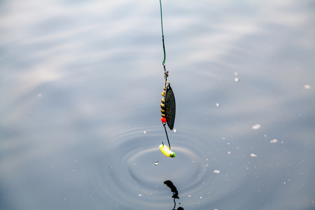 long brass revolving with a long crochet and yellow silicone bait weighs above the surface of the water on a steel leashの写真素材