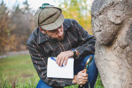 Scientists with a beard in a plaid jacket examines through a magnifying glass stone monument Scythian epoch on a green hillside
の写真素材