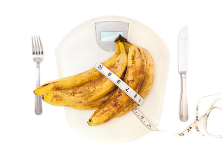 bunch of ripe bananas lay on plastic scales. Around the banana wrapped centimeter. Near fork and knifeの写真素材