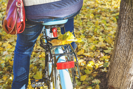 cyclist in jeans sits on a bicycle. On the trunk lies a group of fallen leaves of a maple. Back viewの写真素材