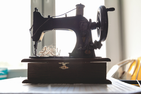 Vintage hand sewing machine and a skein of threads on the background of a closeup window.