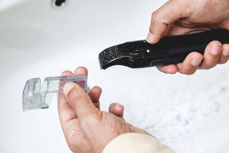 Cleaning the machine for cutting your beard. The man's hands remove the nozzle from the black...