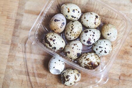 Eggs of quail lie in a transparent box on a wooden board. Near two empty shells.の写真素材