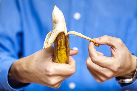 Male hand in a shirt holding a ripe banana and clean it
の写真素材