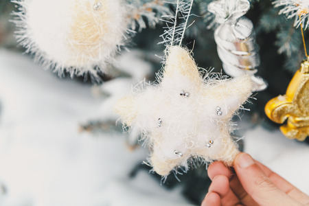 Soft fluffy fur-tree toy in the form of a star weighs in on a snowy coniferous branch. Fingers men held her by the beamの写真素材