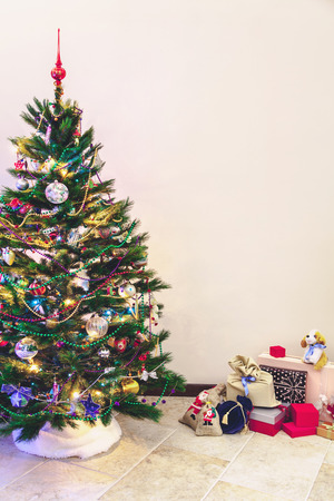 Attributes of the New Year holiday. A dressed tree with toys and garlands stands against a white wall. Near boxes with gifts
の写真素材